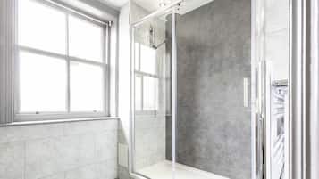 A modern bathroom with a glass-enclosed shower, large windows, and a tiled floor.