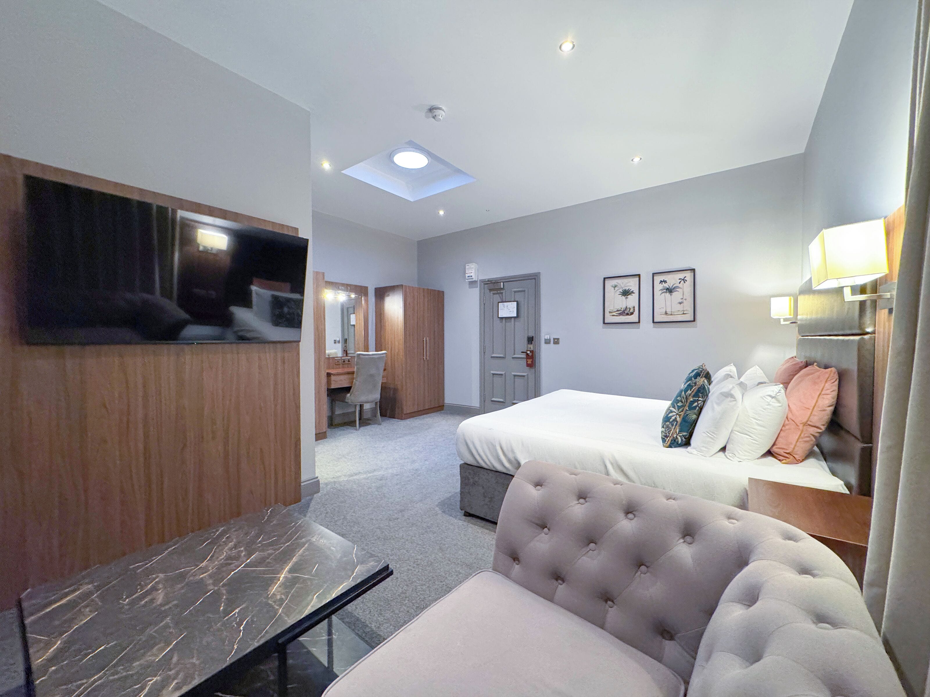 A hotel room with a bed, a desk, a chair, a vanity with a mirror, and a television.
