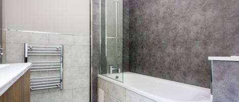 A modern bathroom with a glass-enclosed shower, a white bathtub, and a wooden vanity.