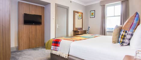 A hotel room with a bed, a television, a desk, and a window.