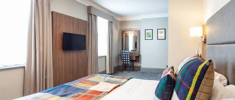 A hotel room with a large bed, a television, a desk, and a chair.