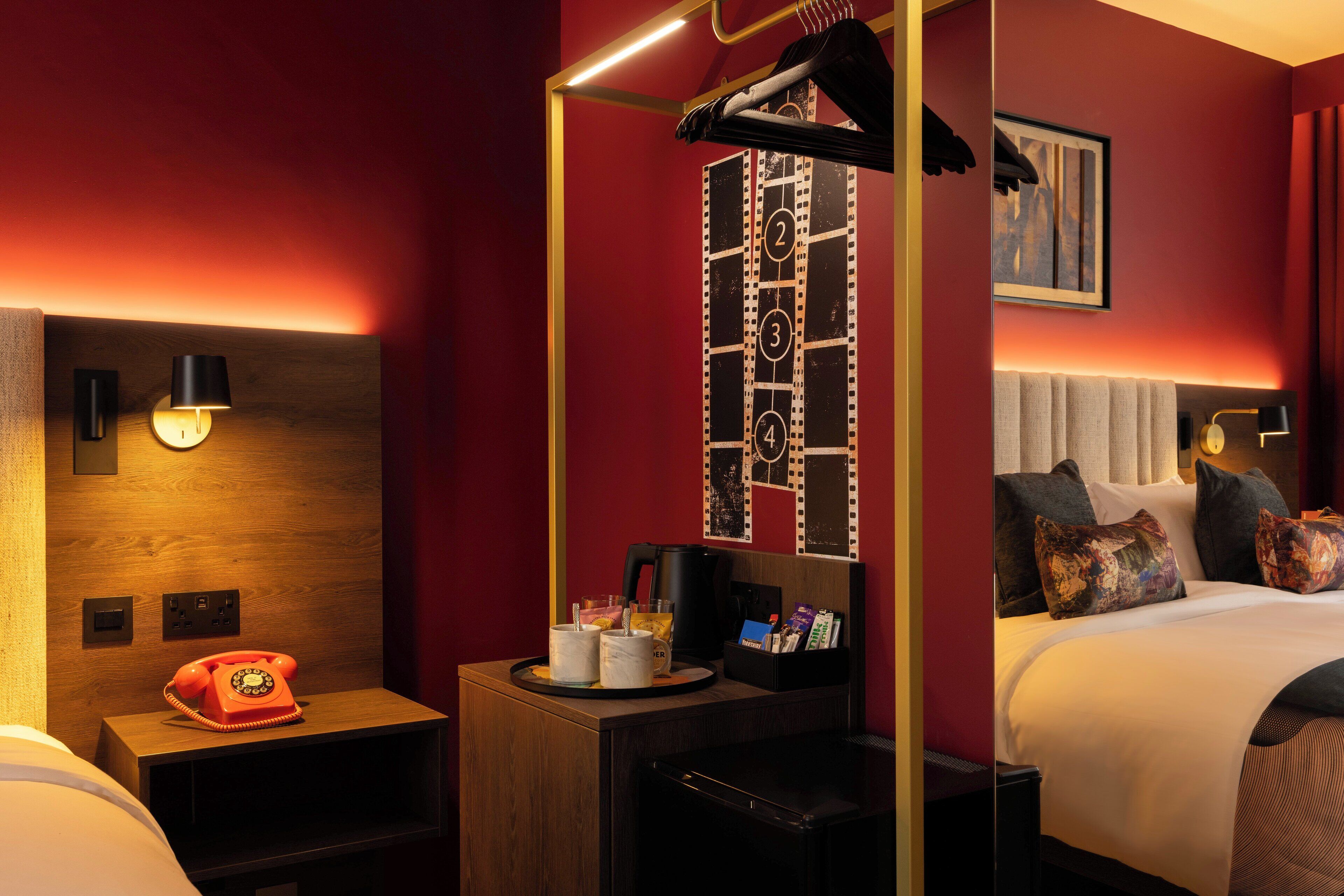A hotel room with a wooden nightstand, a red telephone, a coffee maker, and a tray with cups and a glass.