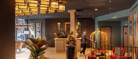 A modern lobby with a reception desk, seating area, and large potted plants.