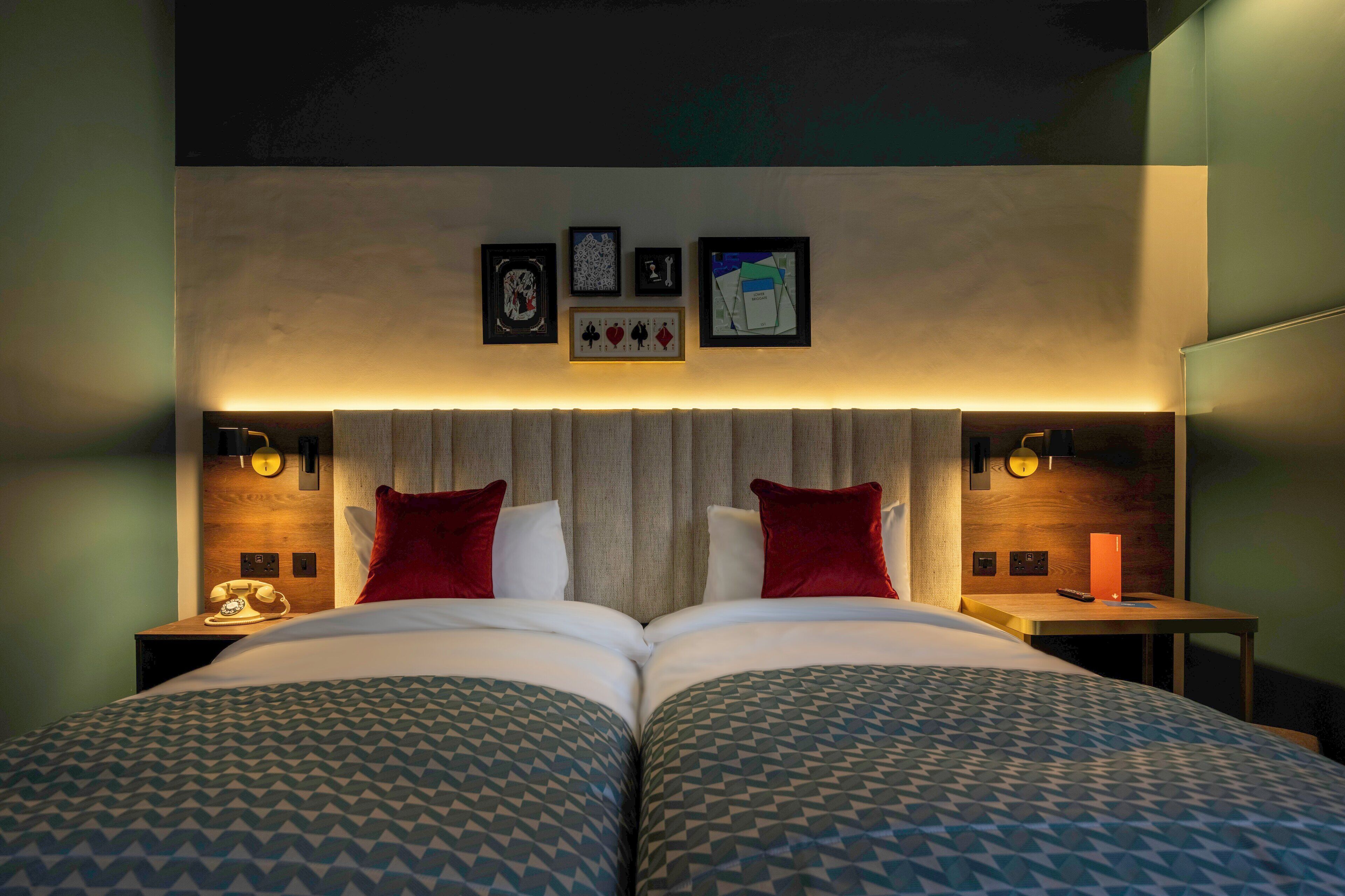 A double bed with patterned bedding, a wooden headboard, and wall-mounted artwork.