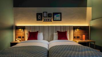 A double bed with patterned bedding, a wooden headboard, and wall-mounted artwork.