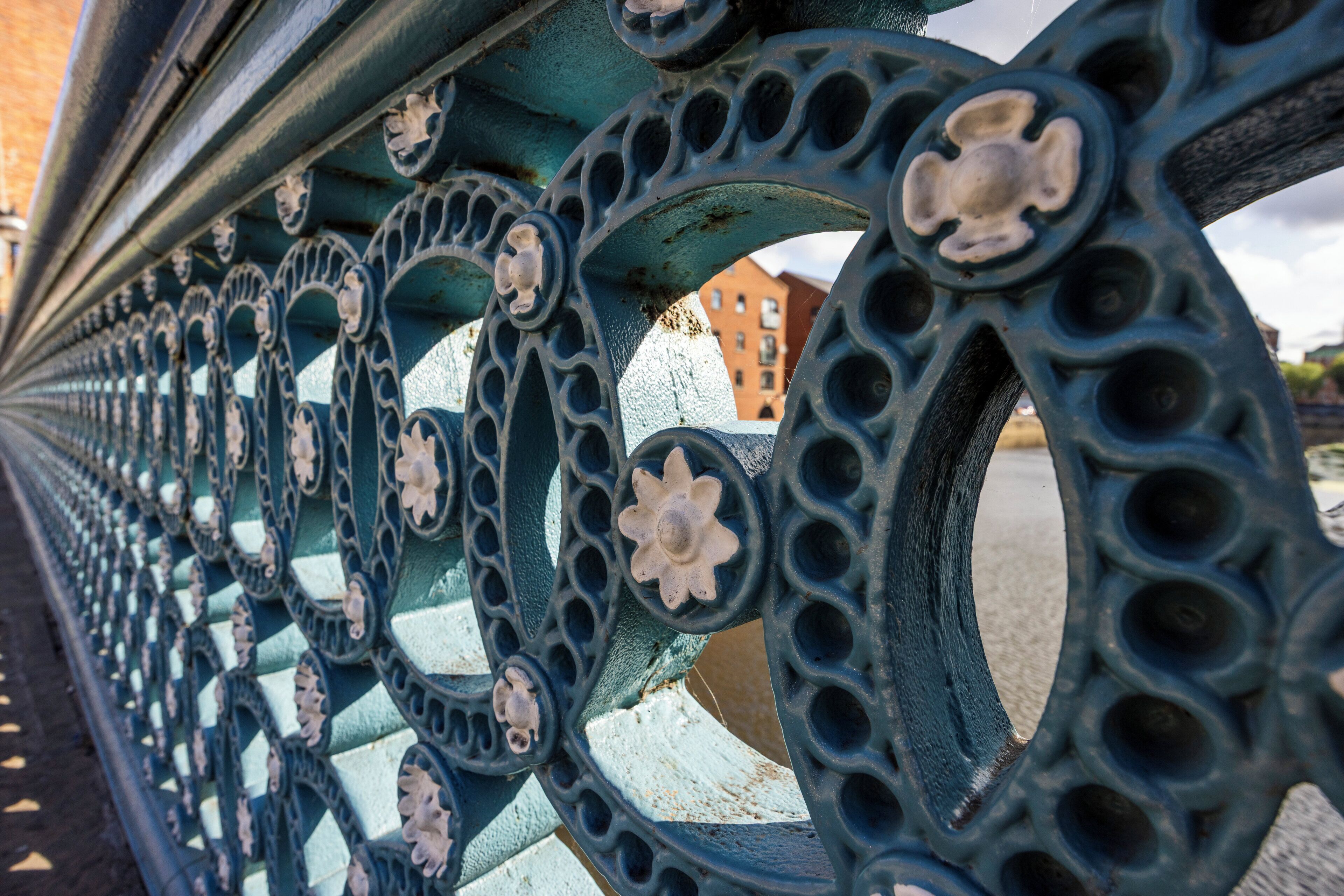 A close-up of a metal fence with decorative floral patterns and circular holes.