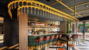 Zona de bar con una lámpara de techo curva, una barra con varias botellas y varios taburetes.