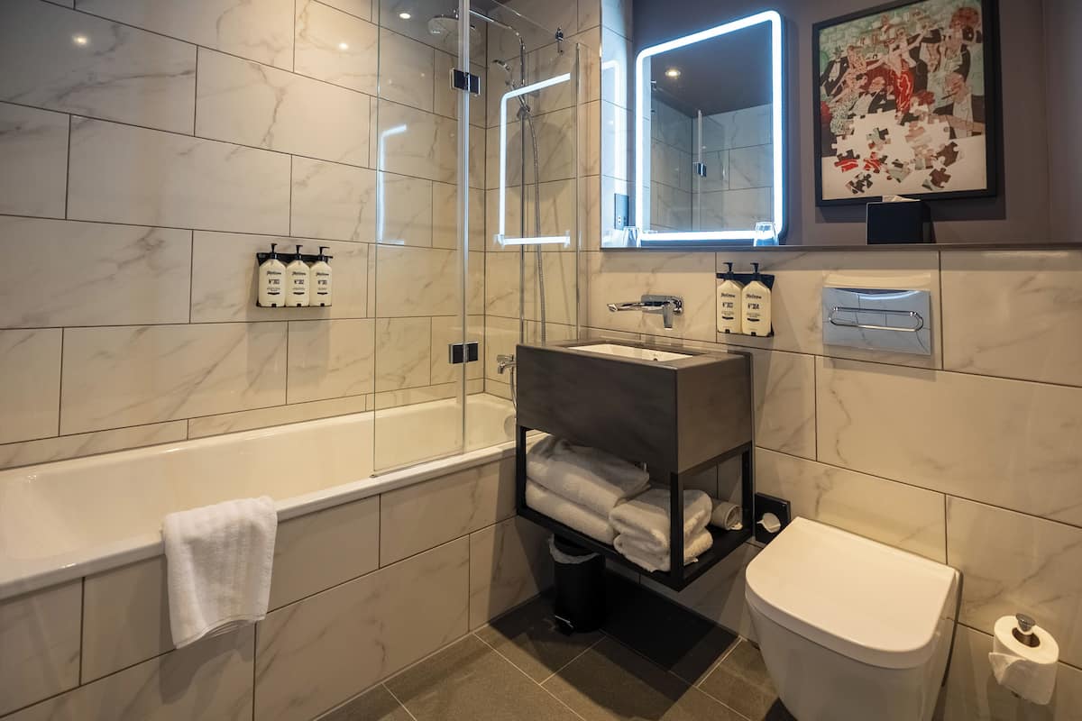 Un baño moderno con suelo de baldosas de mármol, una bañera blanca, un inodoro y un lavabo con un perchero para toallas.