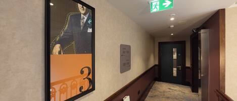 A hotel hallway with a framed portrait, a directional sign, and a door.