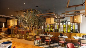 Un restaurante con suelo de madera, una zona de estar con sofá y sillas, y un árbol grande en el centro.