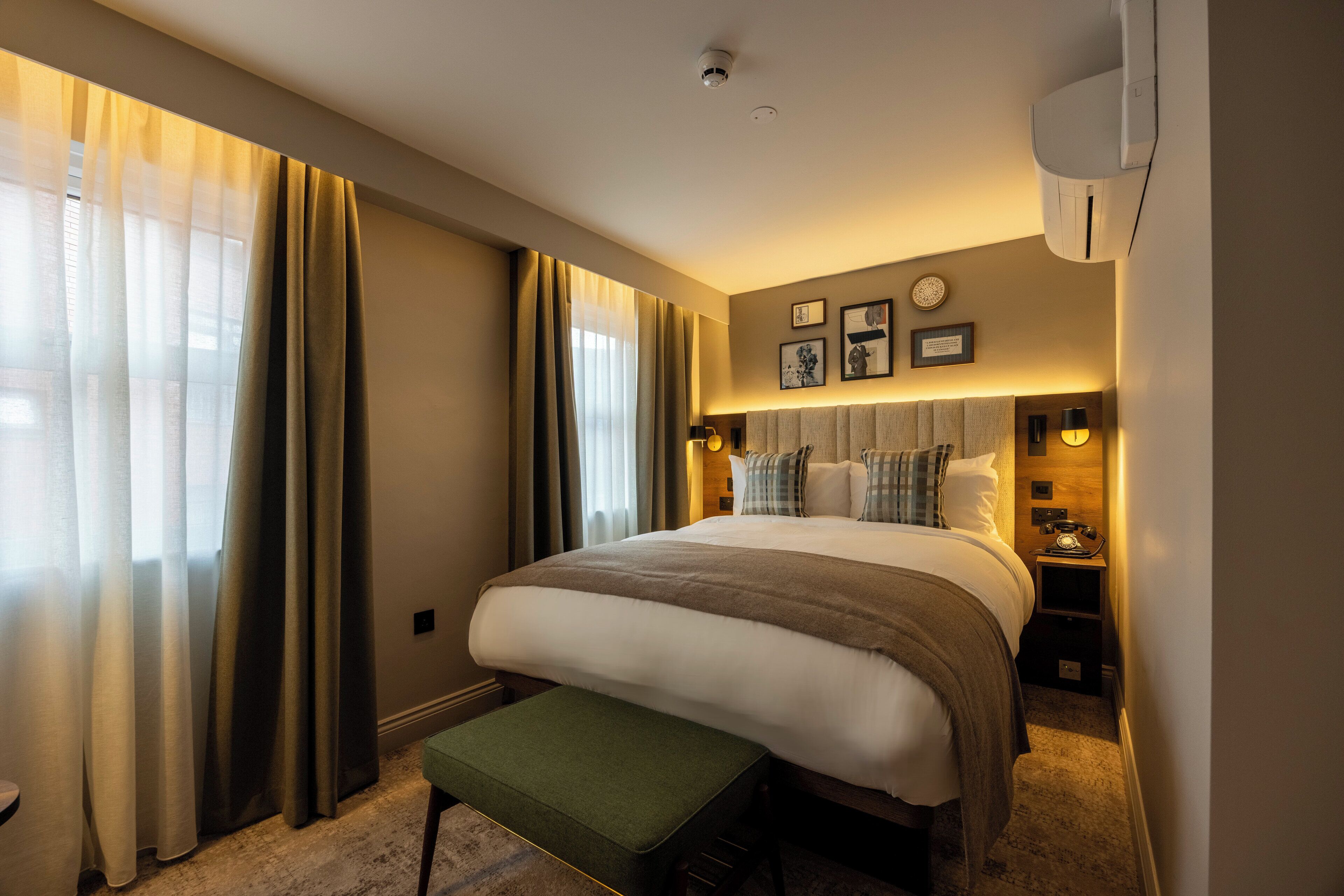 Ein Hotelzimmer mit einem großen Bett, einem Nachttisch, einer Lampe und einer Wandklimaanlage.