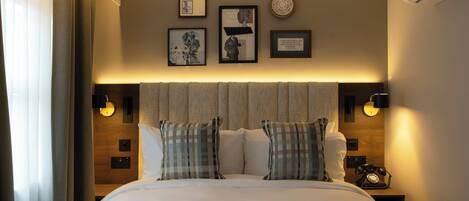 A neatly made bed with plaid pillows, a headboard with wall-mounted lights, and framed artwork on the wall.