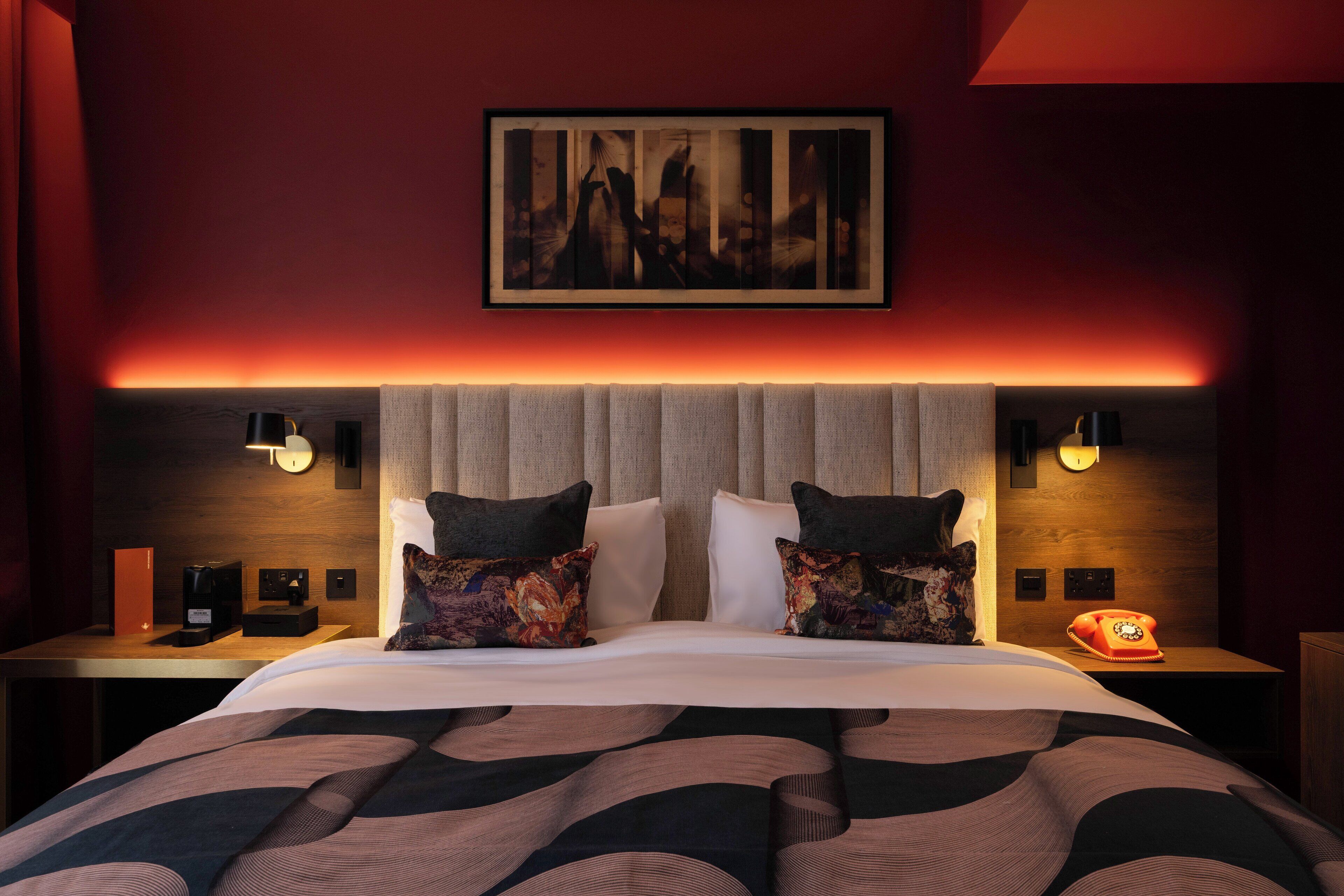 A hotel room with a large bed, two bedside tables, a nightstand, a telephone, and a wall-mounted artwork.