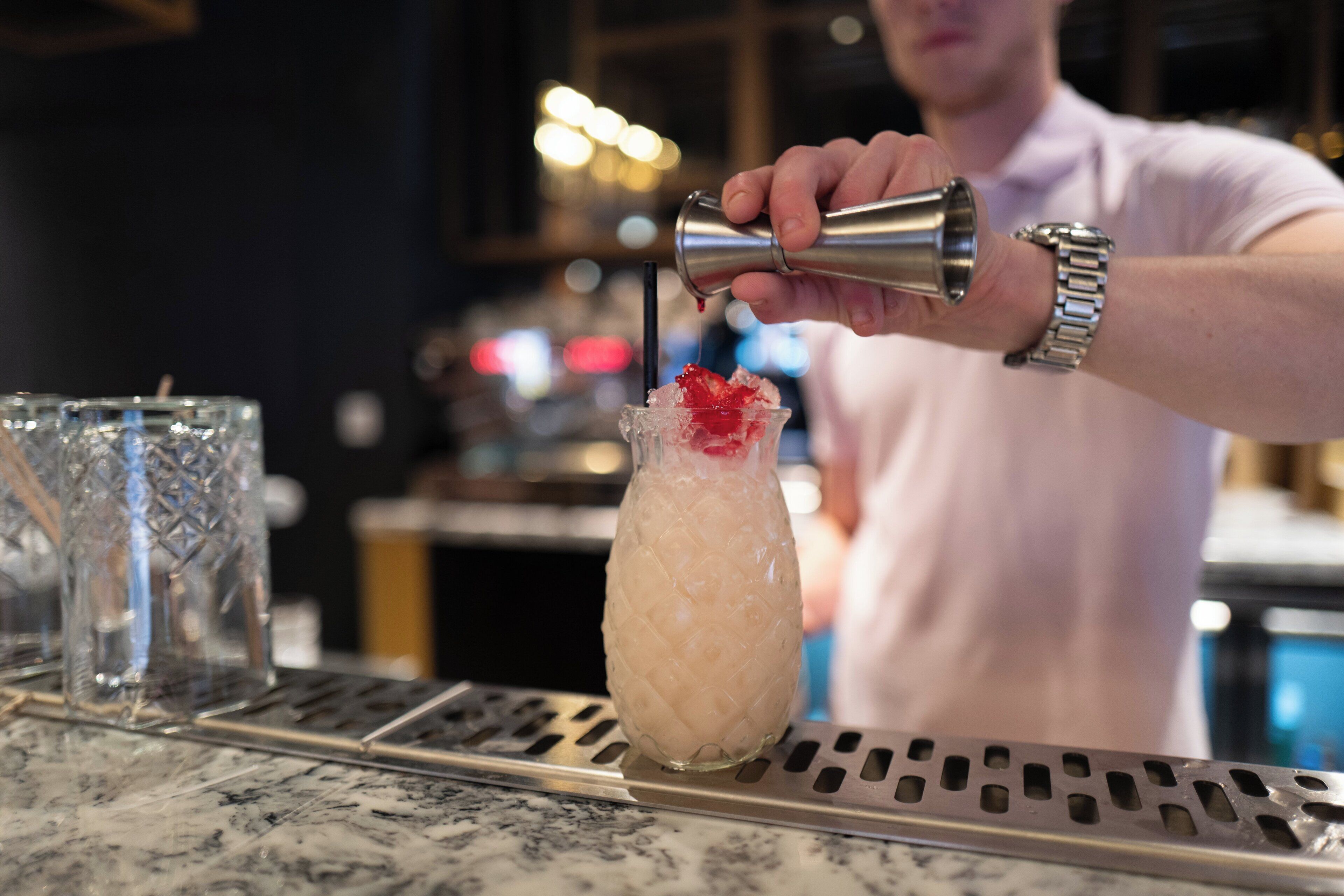 A bartender pouring a drink into a glass with a red garnish.