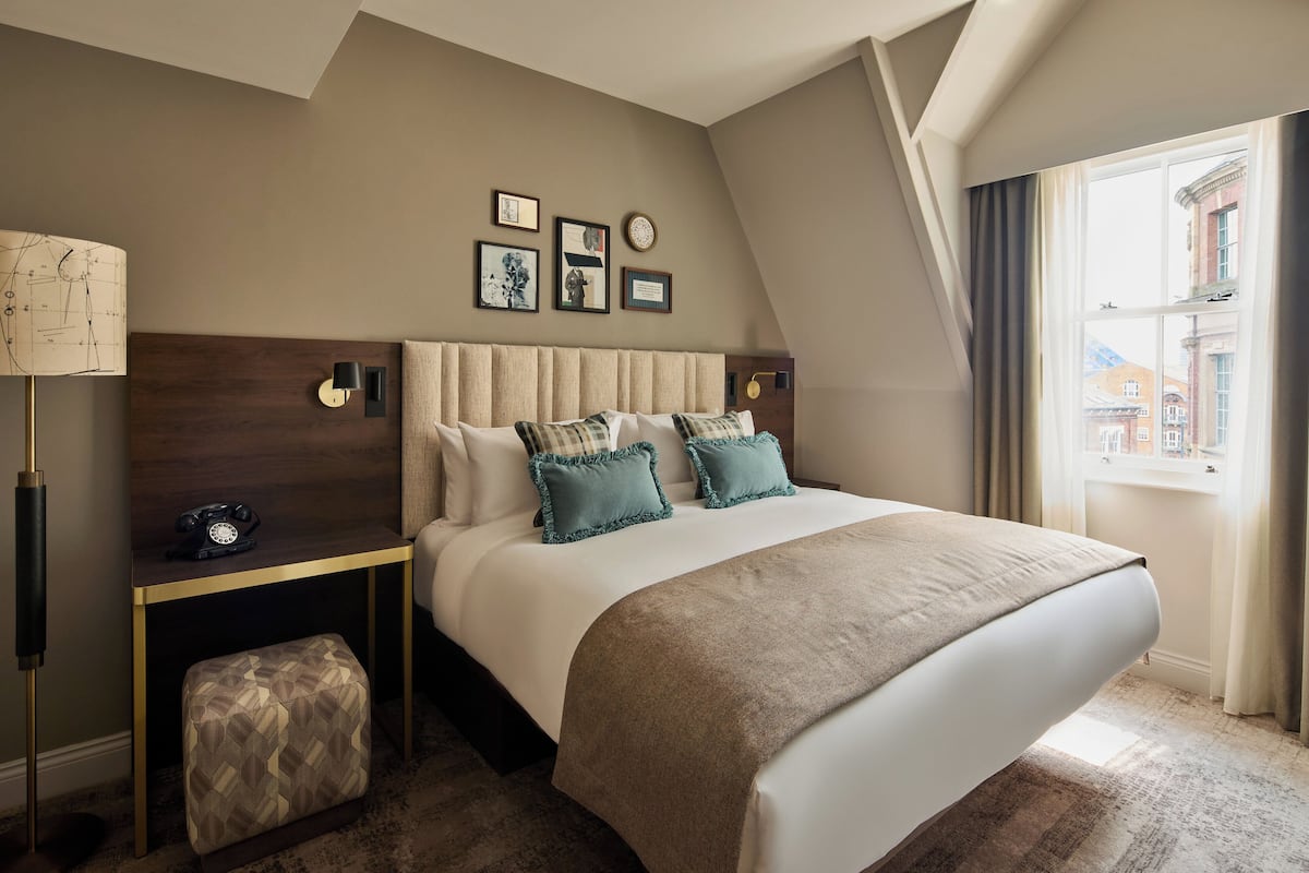 Un dormitorio con una cama grande, una mesita de noche, una lámpara y una ventana con cortinas.