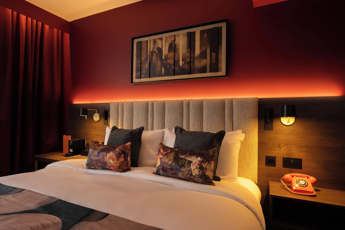 A hotel room with a large bed, two decorative pillows, a nightstand with a telephone, and a wall-mounted light fixture.