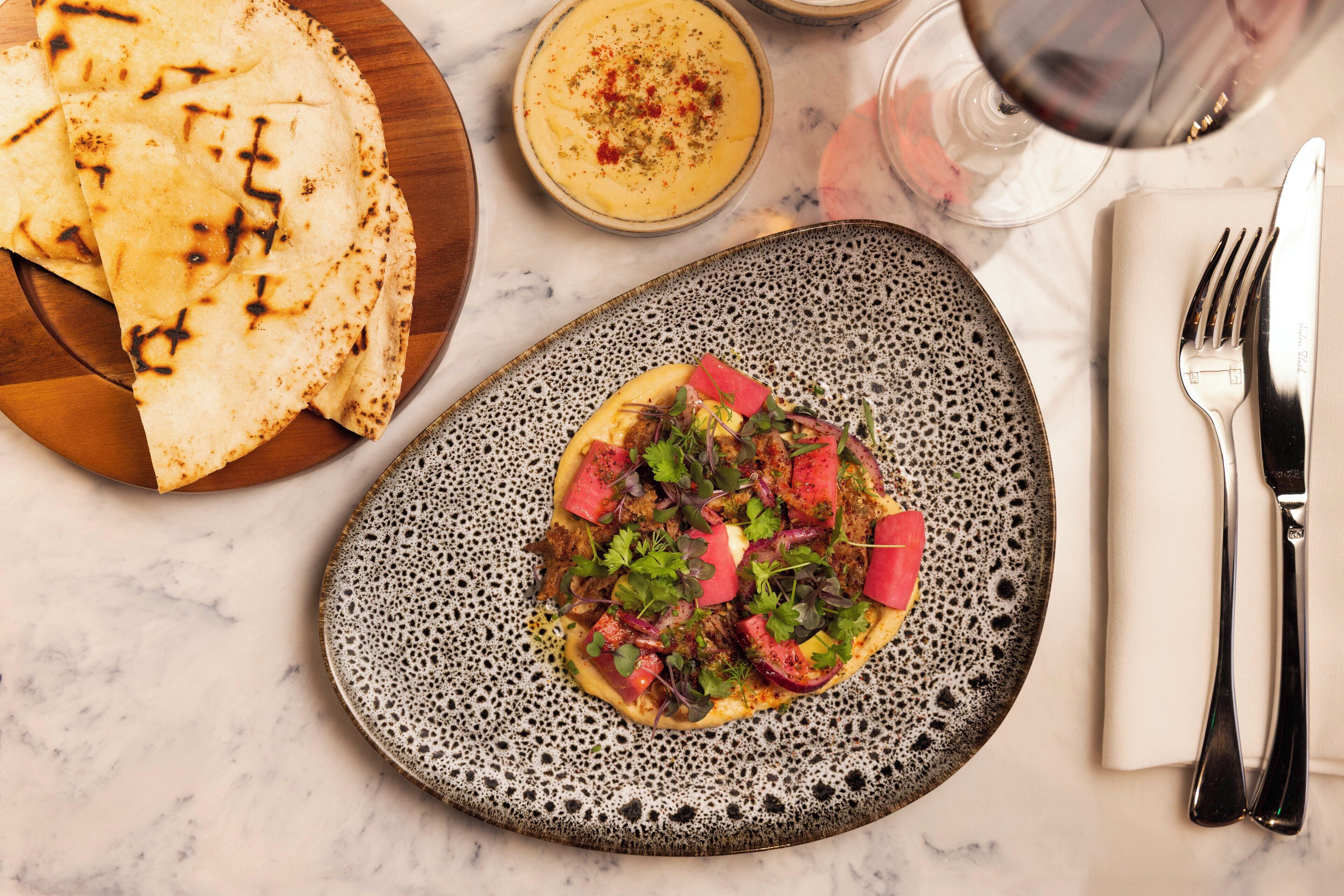 A plate of food with a variety of toppings, a bowl of soup, and a glass of red wine on a marble table.