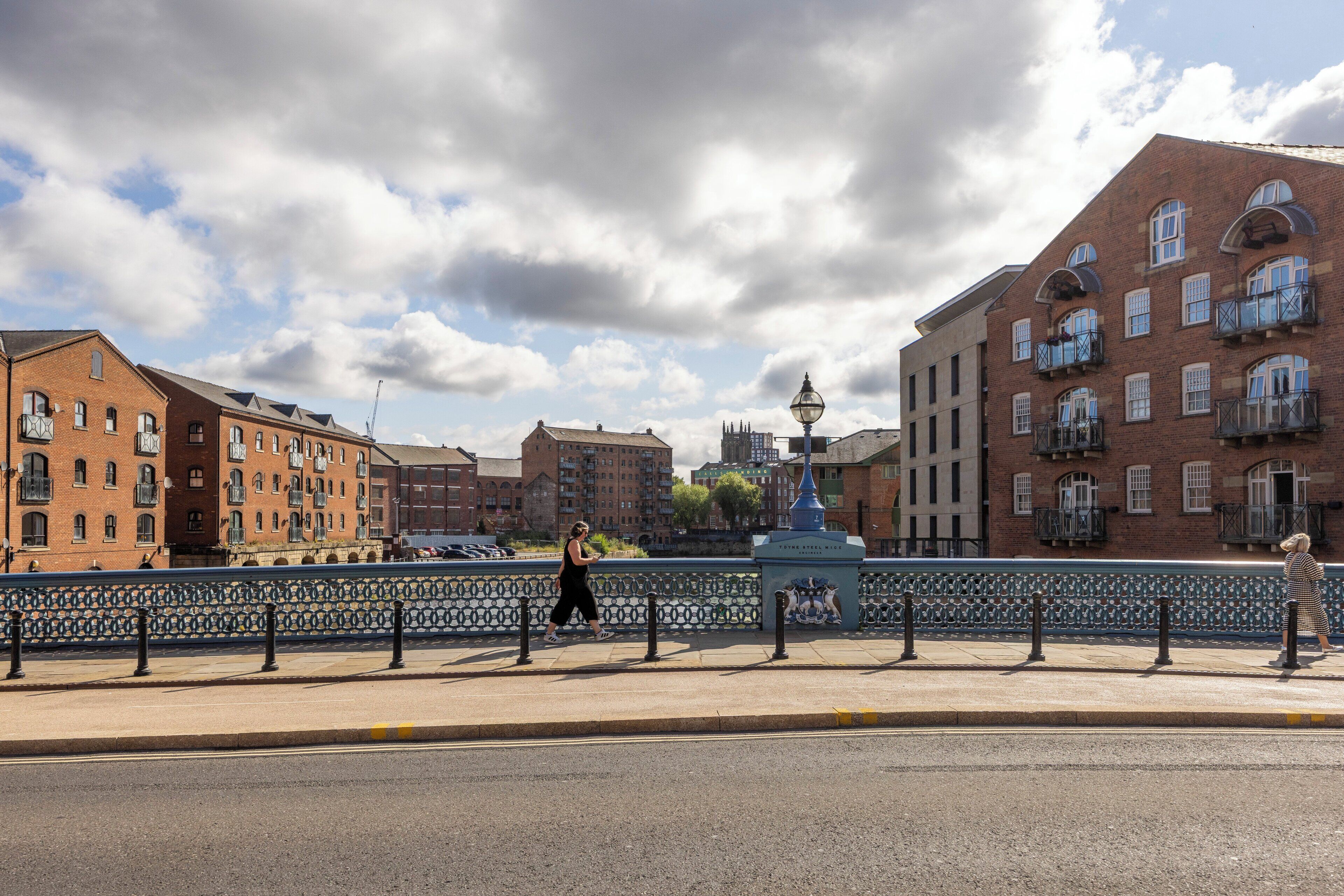 A pedestrian bridge with a decorative fence, a statue, and buildings with multiple stories and balconies.