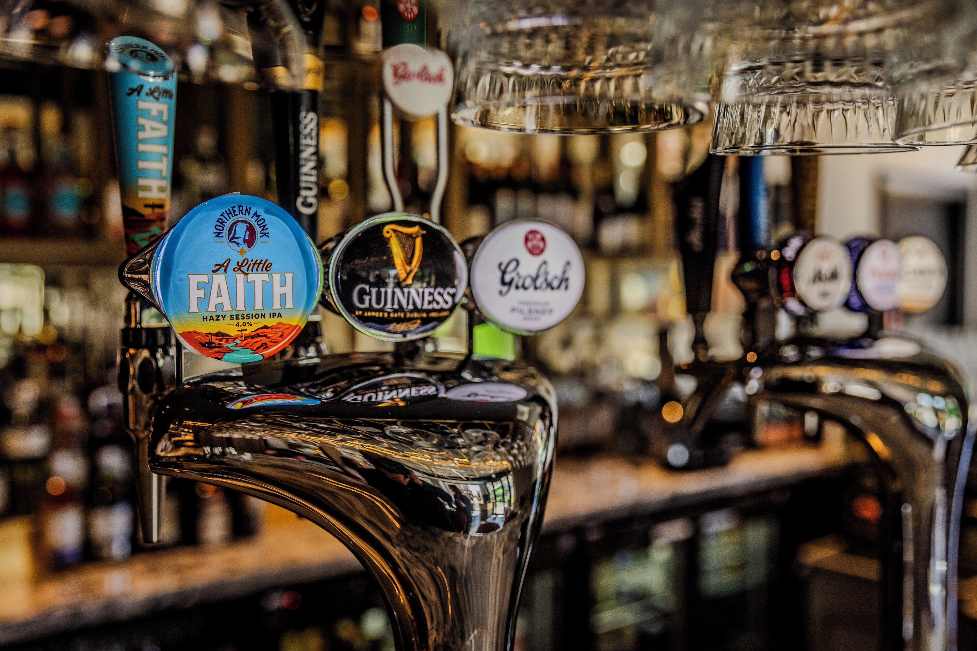 Ein Zapfhahn an einer Bar mit verschiedenen Biersorten, darunter Northern Monk, A Little Faith, Guinness und Grolsch.