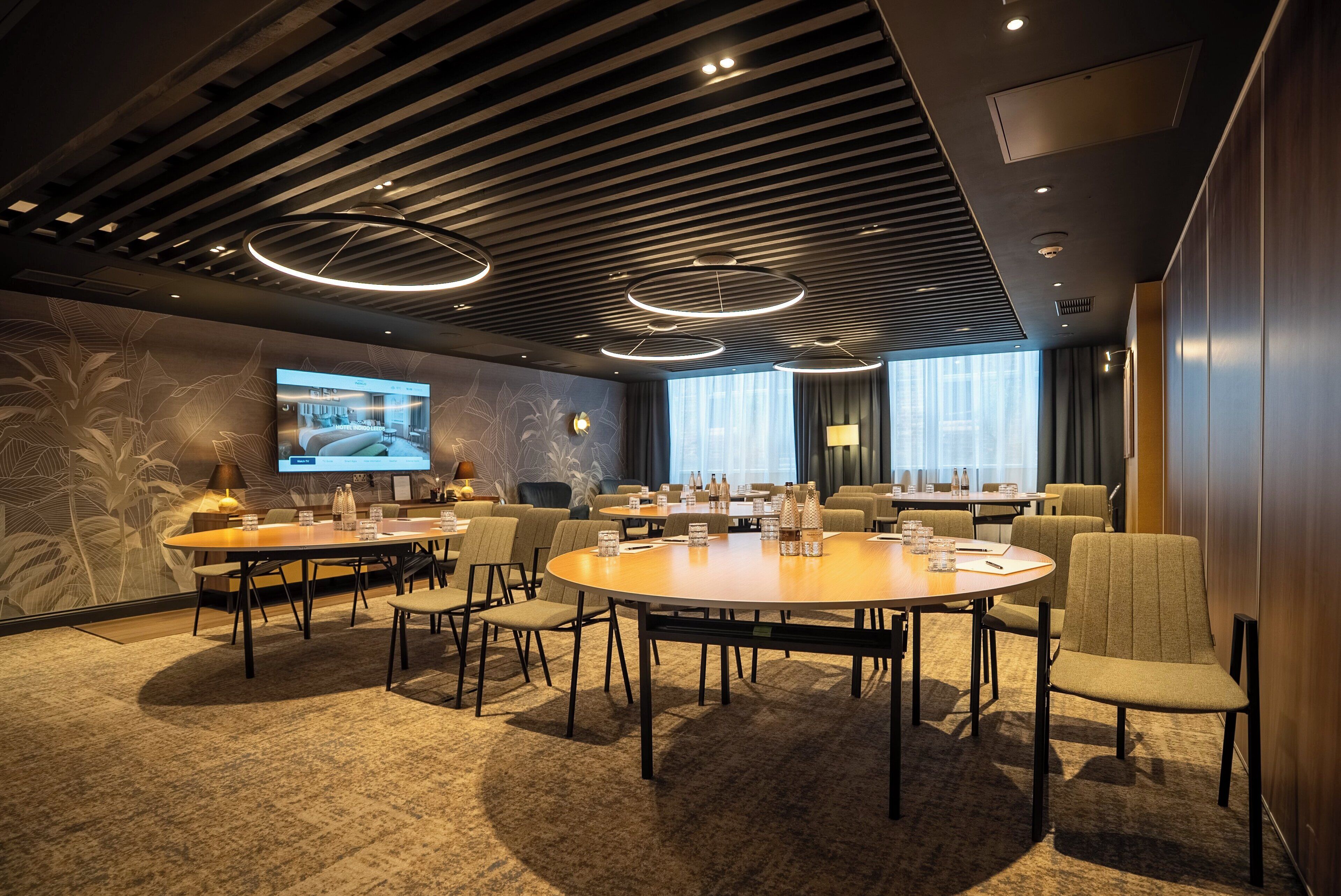 A modern conference room with a large table, multiple chairs, and a television screen.