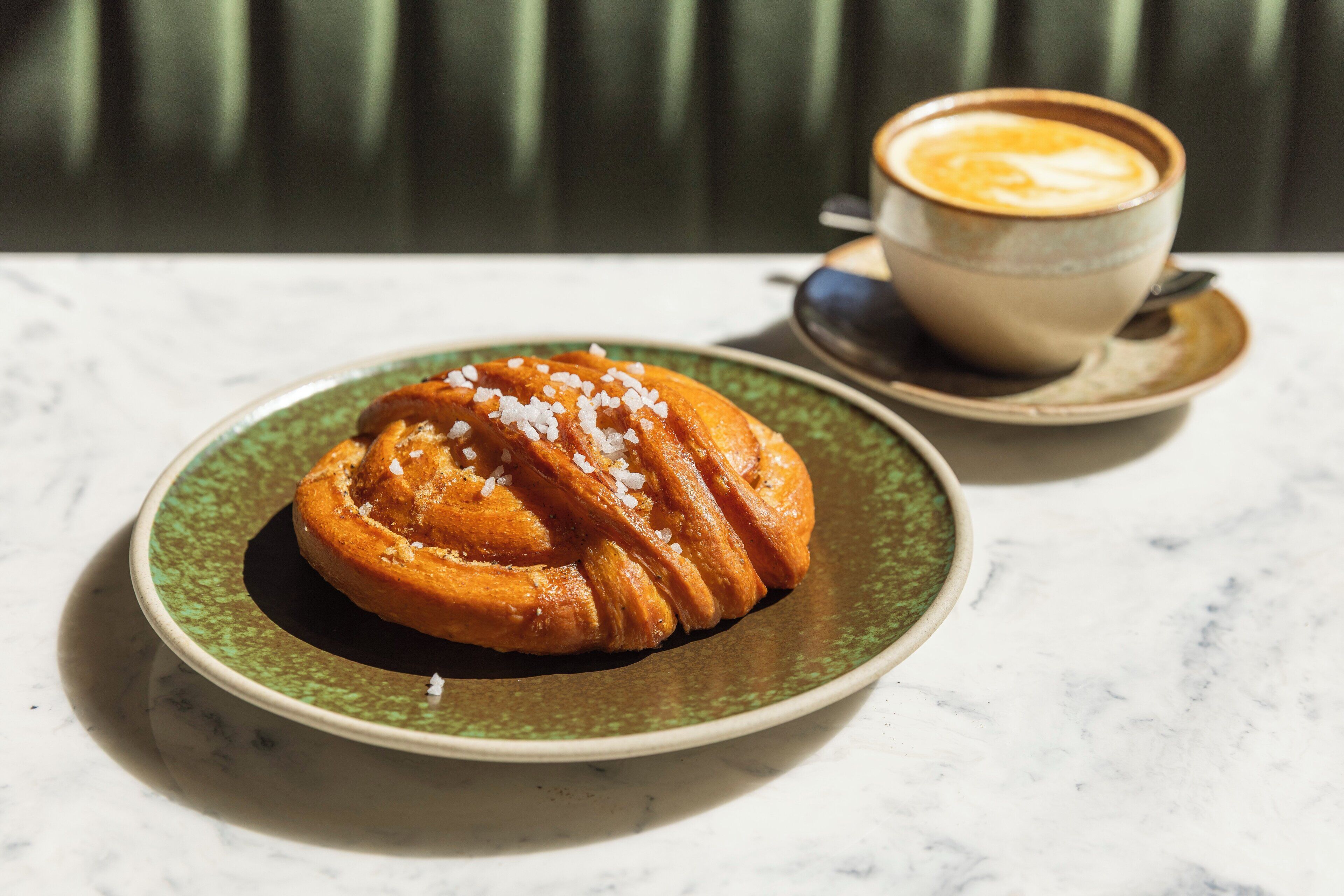 A pastry on a plate with a cup of coffee on a saucer.