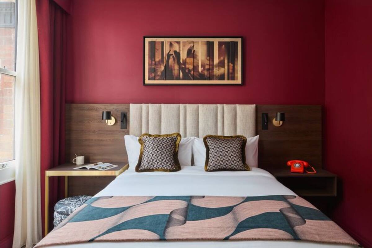 Habitación de hotel con una cama grande, una mesita de noche con teléfono, un cuadro enmarcado en la pared y una ventana con cortinas.