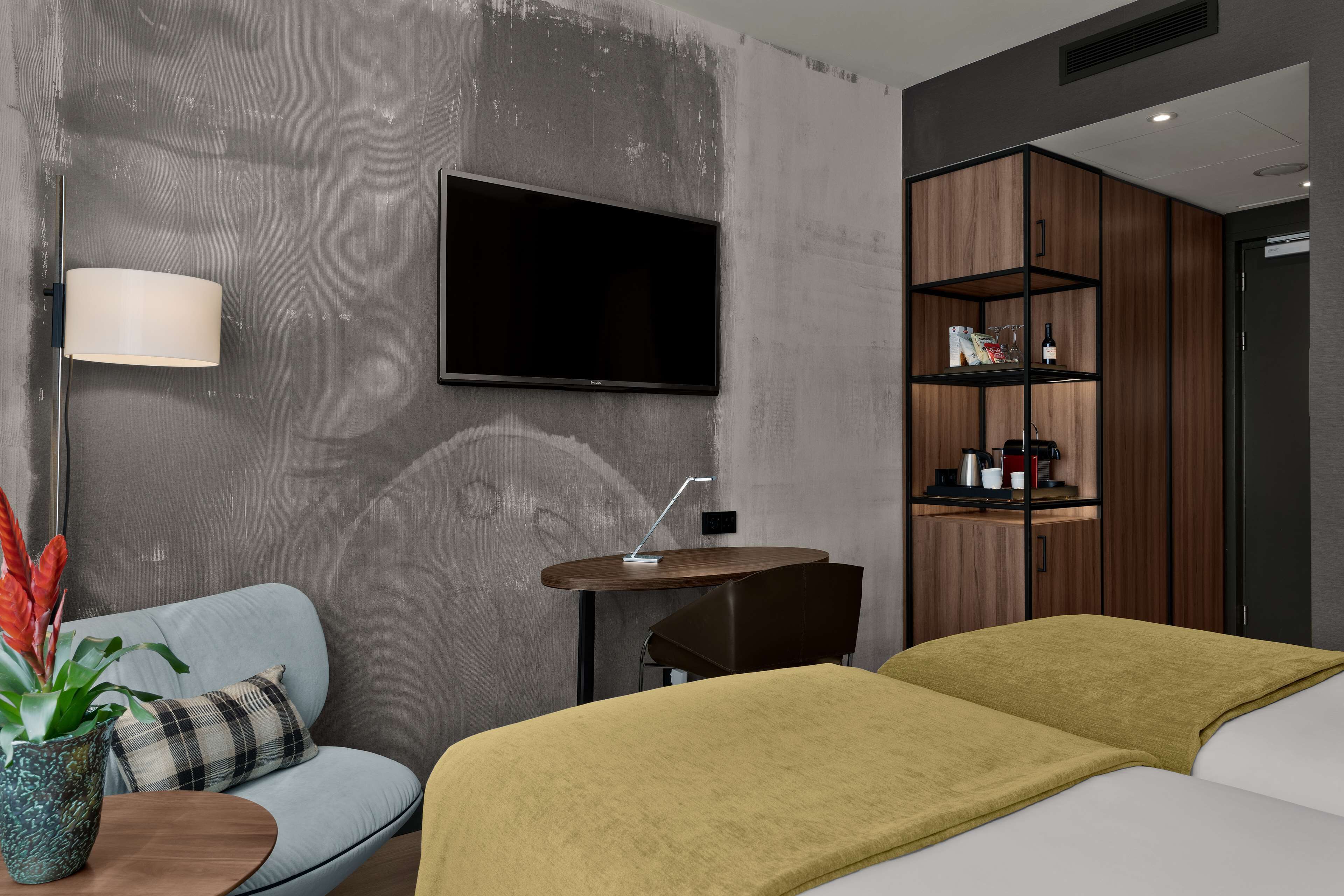 Una habitación de hotel moderna con sofá, cama, televisor, una mesita y una estantería.