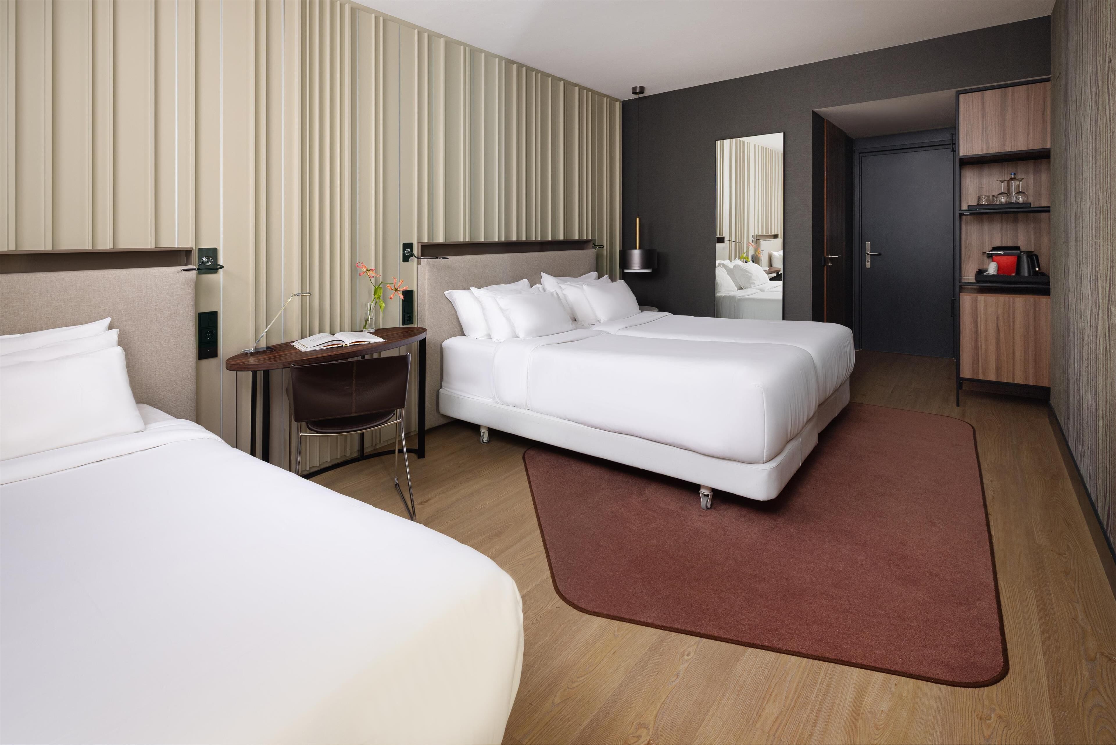 A hotel room with two beds, a desk, a mirror, and a wardrobe.