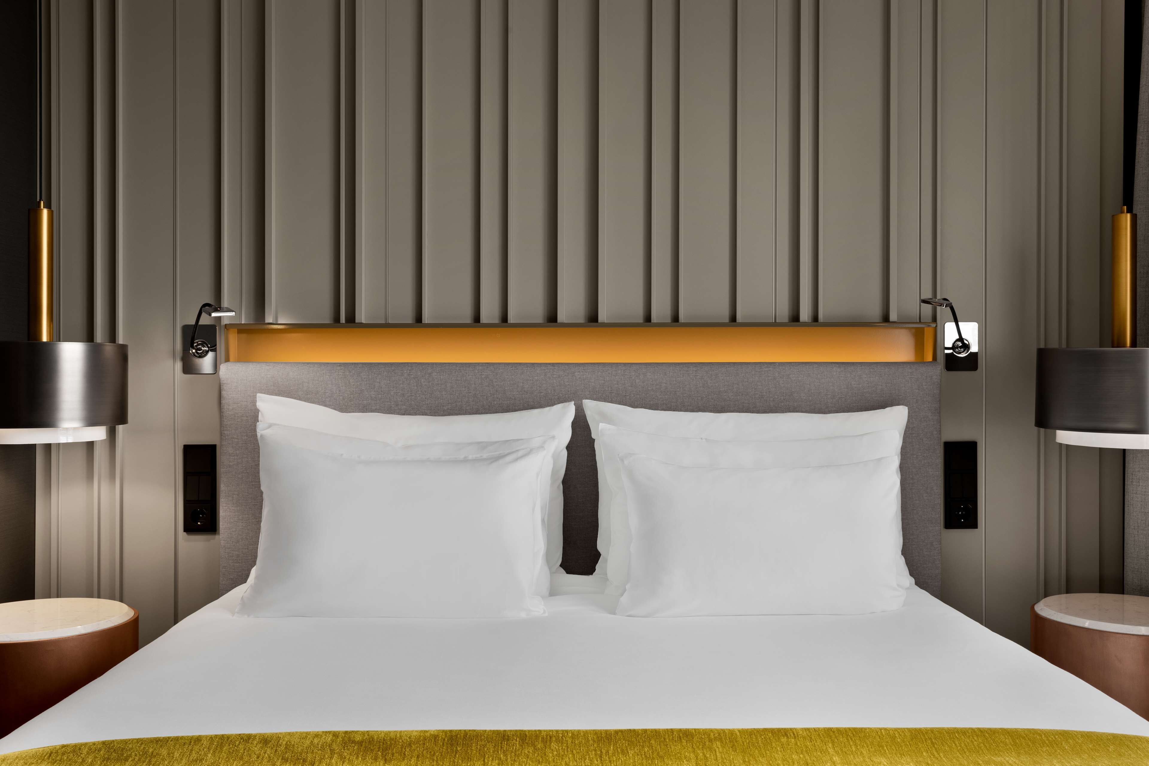 A modern hotel room with a large bed, two bedside tables, and a headboard with integrated lighting.