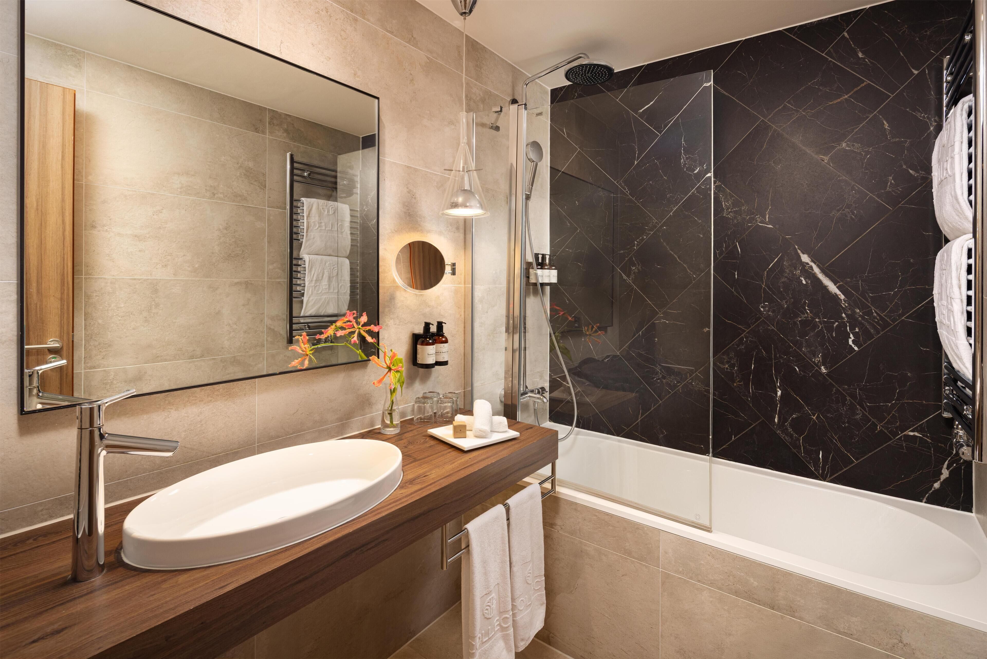Un baño moderno con un espejo grande, un tocador de madera, un lavabo blanco, una ducha con pared de mármol negro y un perchero para toallas.