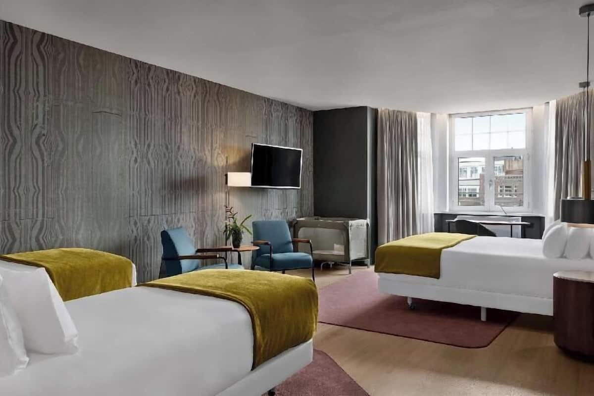 A hotel room with two beds, a desk, a chair, a TV, and a window with curtains.