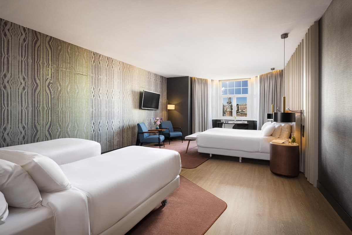 A modern hotel room with two beds, a TV, a desk, and a view of a cityscape.
