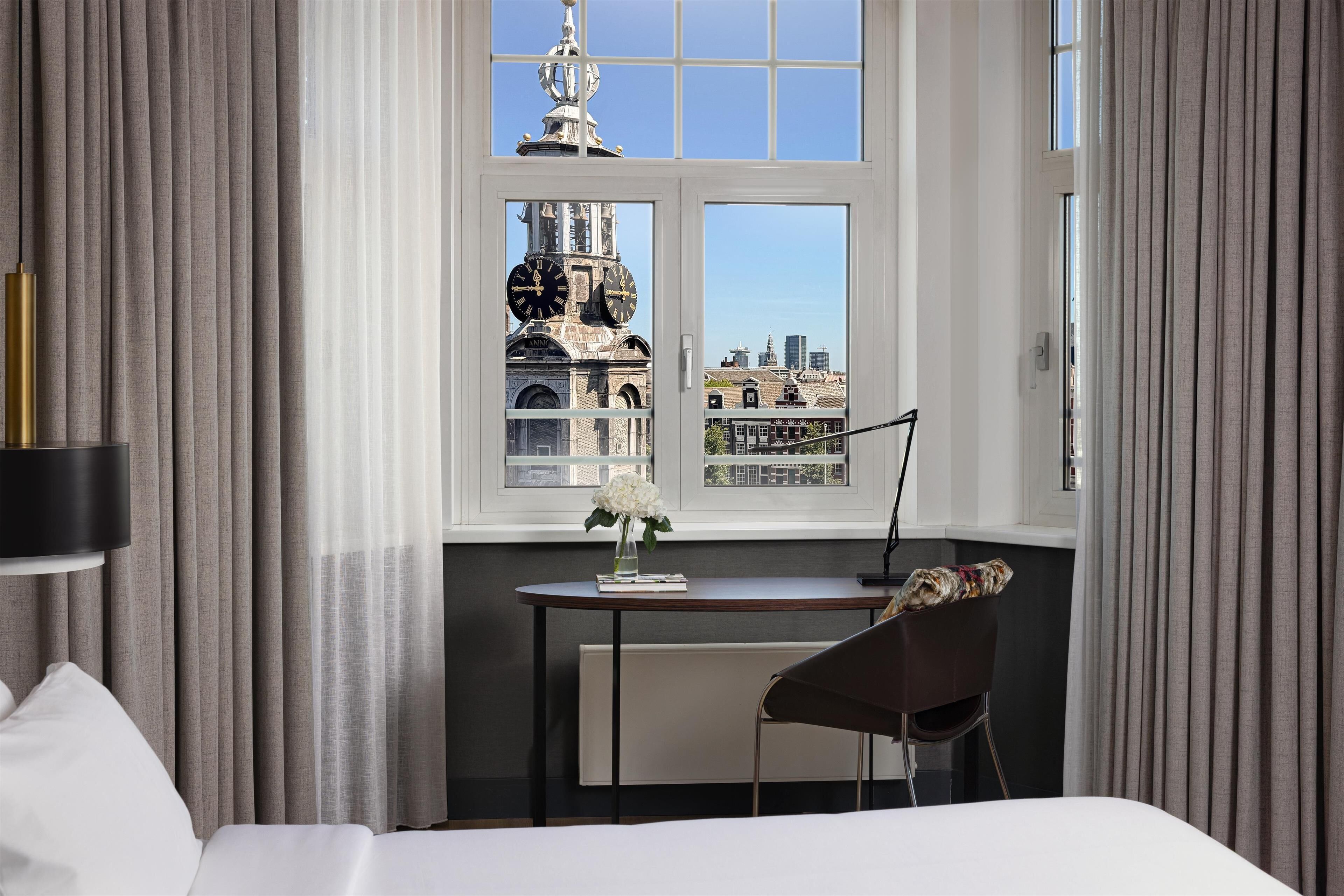Une chambre d’hôtel avec une grande fenêtre, un bureau, une chaise et un lit.