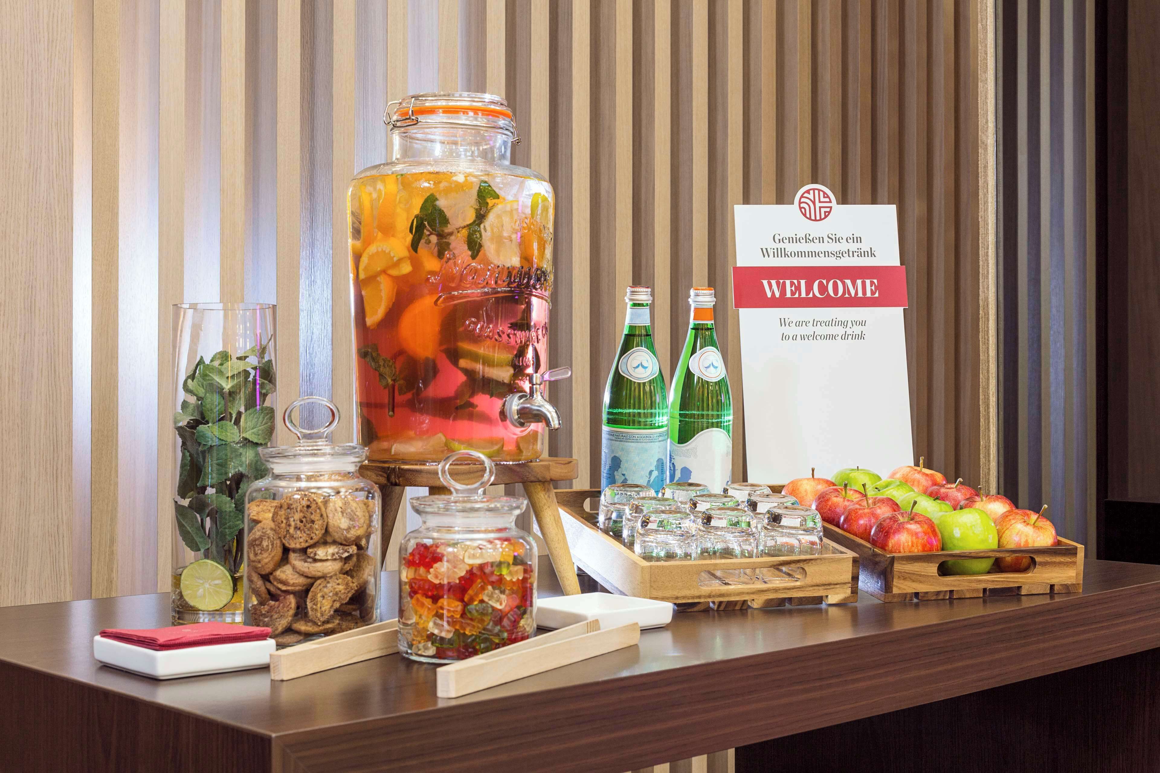 A welcome drink station with a large pitcher, jars of cookies, and a tray of apples.