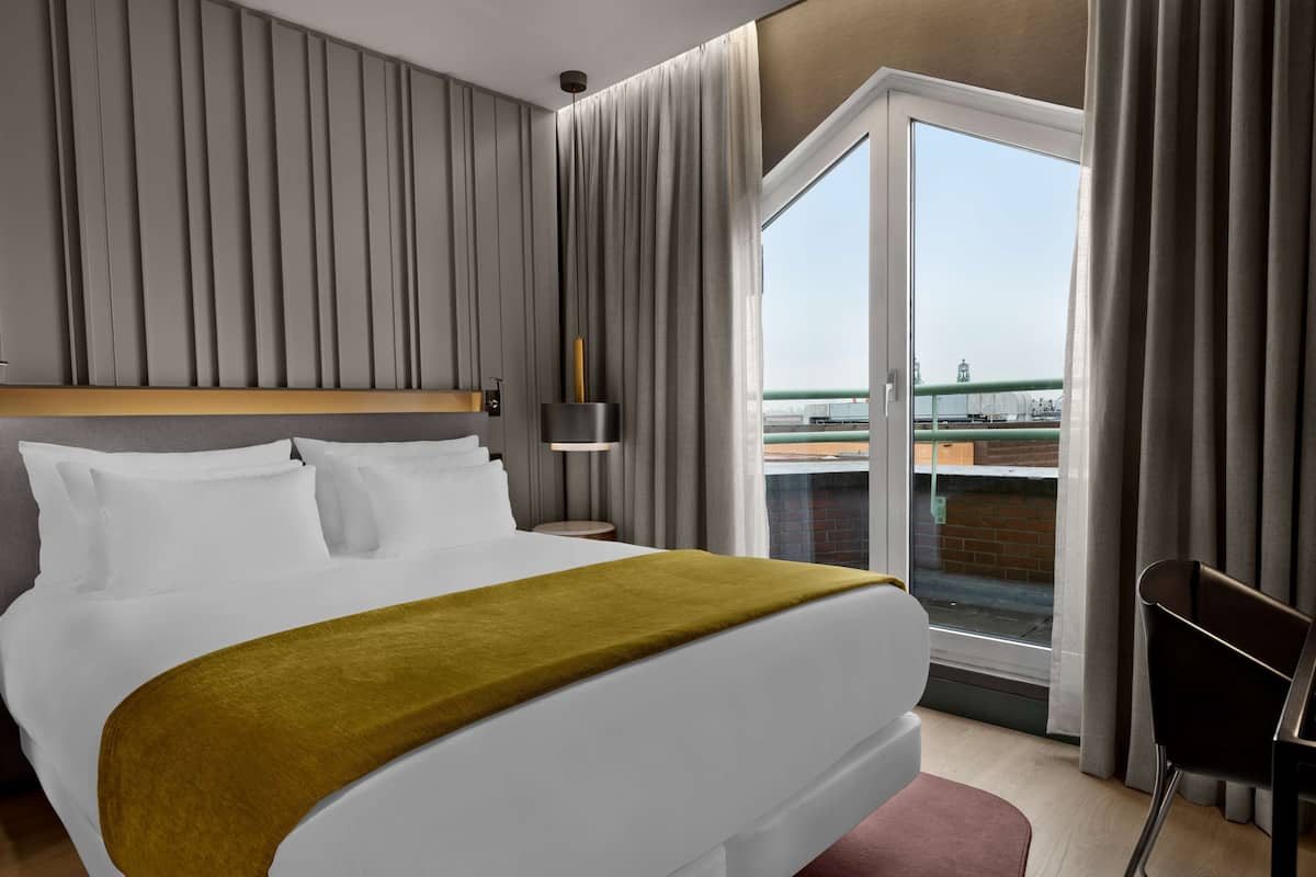 A hotel room with a large bed, a nightstand, a lamp, and a view of a bridge through the window.