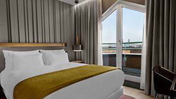 Habitación de hotel con una cama grande, una mesita de noche, una lámpara y vistas a un puente por la ventana.