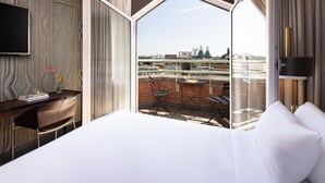 Habitación de hotel con una cama grande, un escritorio con silla, un televisor y un balcón con vista a la ciudad.