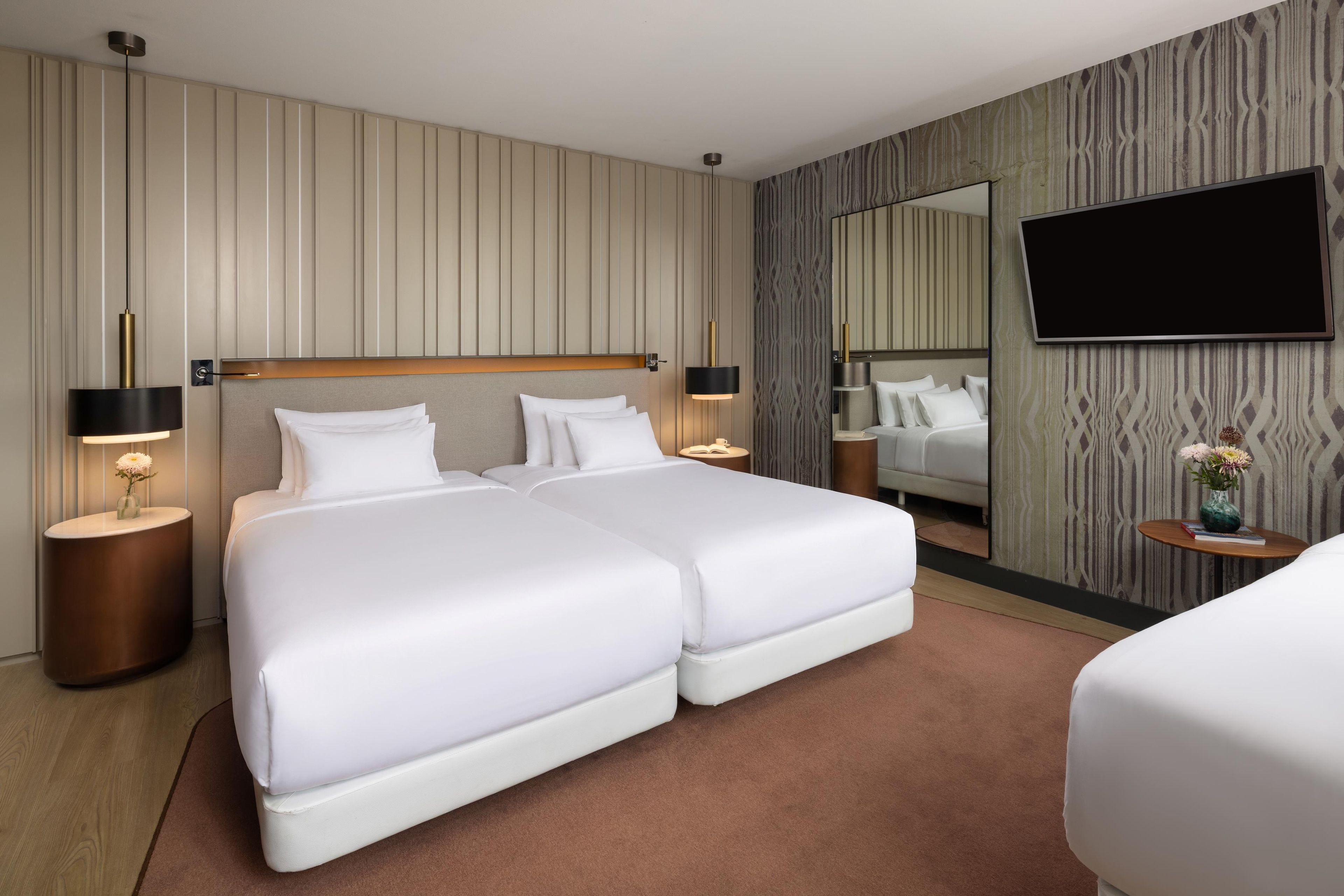 Une chambre d’hôtel avec un grand lit, deux tables de chevet, un téléviseur à écran plat et un miroir au mur.
