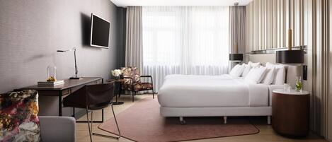 Una habitación de hotel moderna con una cama grande, un escritorio, una silla, un televisor y una mesita de noche con una lámpara.
