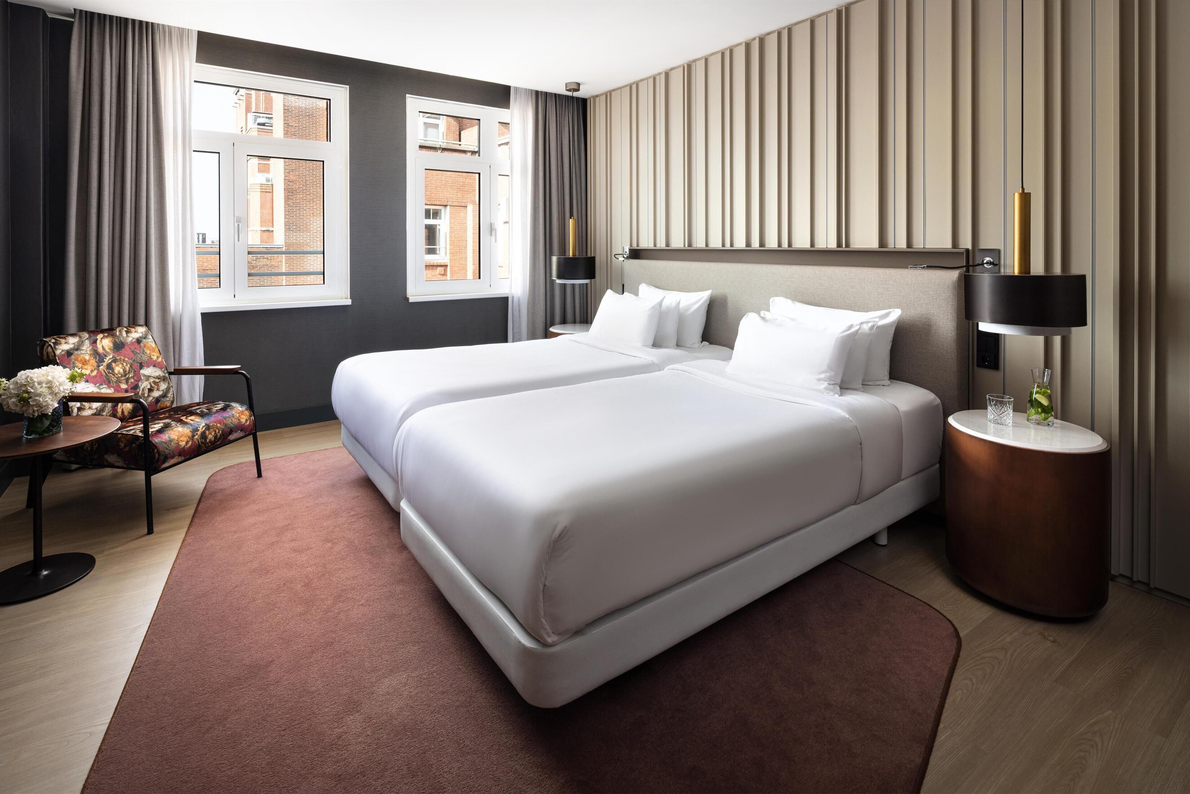 Une chambre d’hôtel avec deux lits, une petite table ronde, une chaise et une vue sur la ville par la fenêtre.