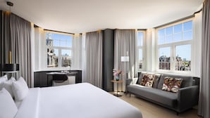 Una habitación de hotel moderna con una cama grande, un sofá, un escritorio y vistas a la ciudad.