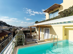 Una piscina en la azotea con vistas a un paisaje urbano, una zona de estar cubierta y un cielo despejado.