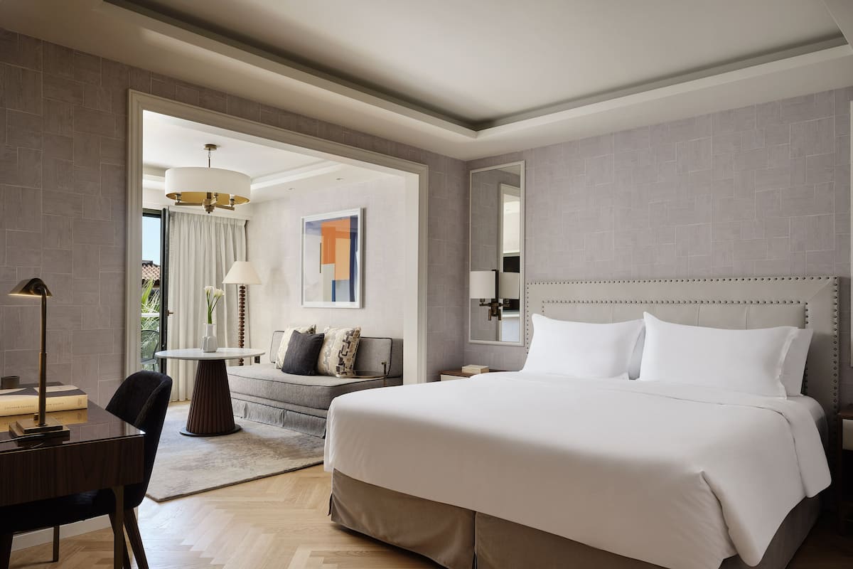 A modern hotel room with a large bed, a desk, a chair, and a sofa.