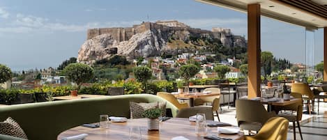 Restaurante con terraza al aire libre con vistas a una fortaleza histórica. Las mesas están dispuestas con cubiertos y vasos.
