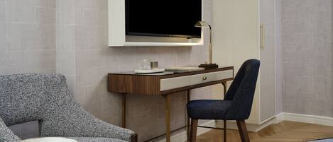 Una habitación moderna con una televisión de pantalla plana montada en la pared, un escritorio con una lámpara, una silla y una mesita con un cuenco.