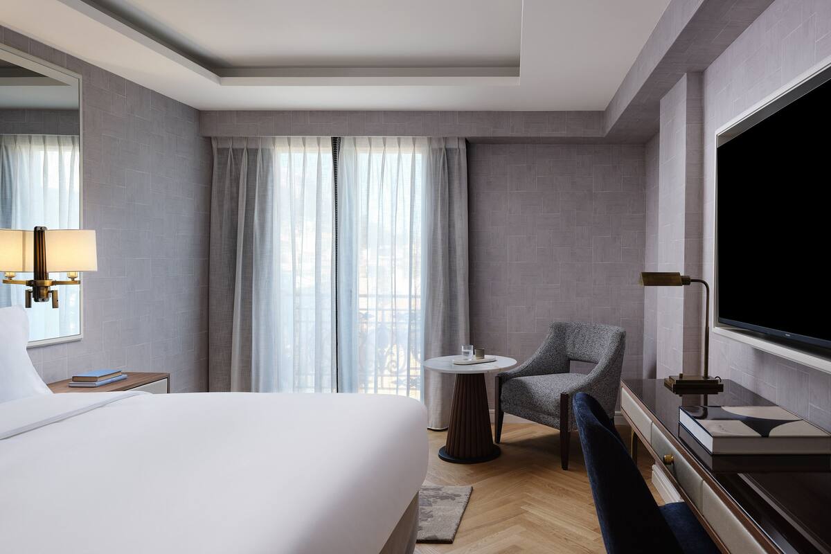 A hotel room with a bed, a chair, a round table, a TV, and a window with curtains.