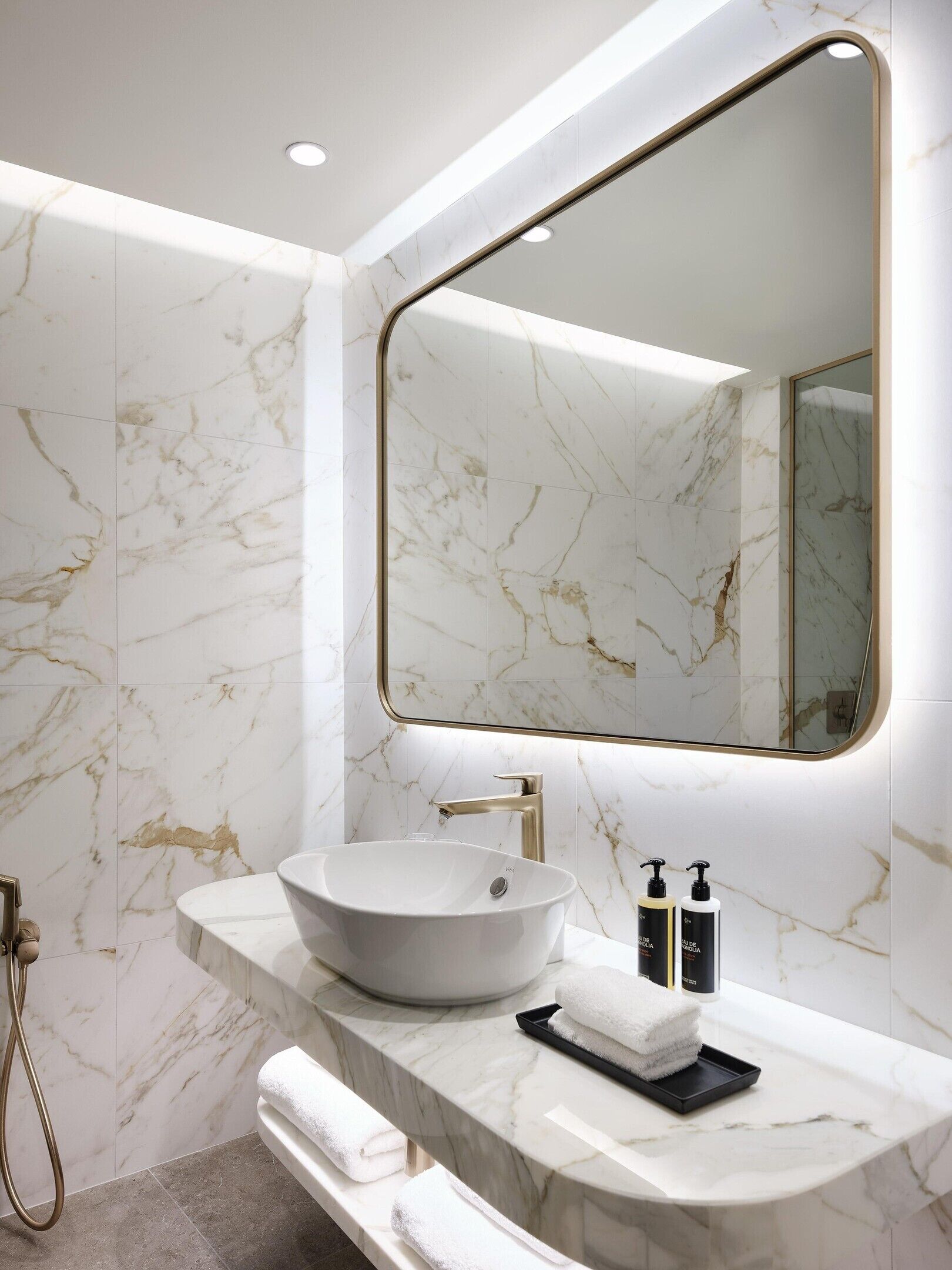 A bathroom with a marble vanity, a large mirror, and a handheld showerhead.