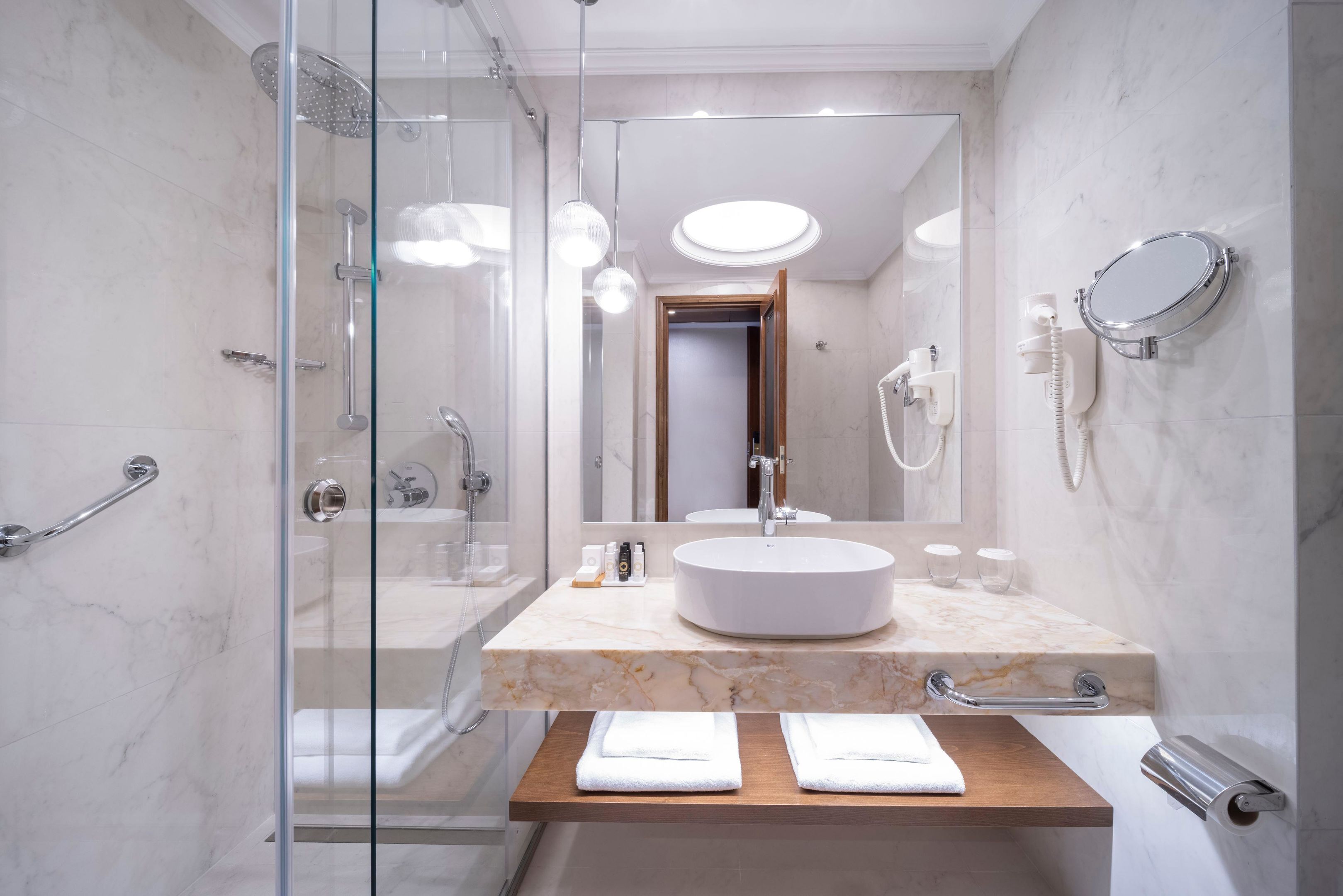 Une salle de bain moderne avec une douche à parois de verre, un comptoir en marbre, un lavabo et un miroir.