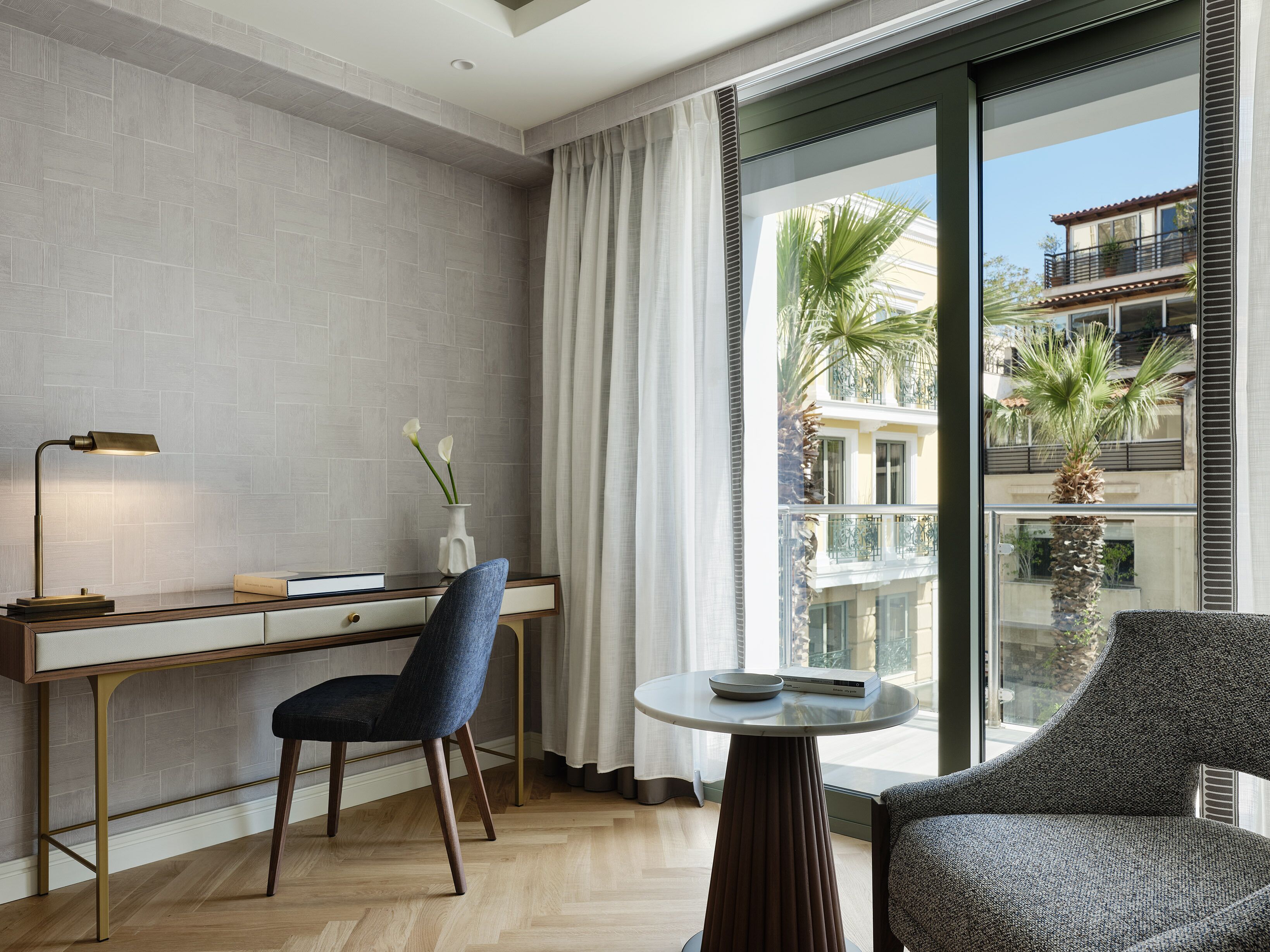 A modern hotel room with a desk, chair, and a round table with a book and a bowl.