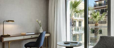 A modern hotel room with a desk, chair, and a round table with a book and a bowl.